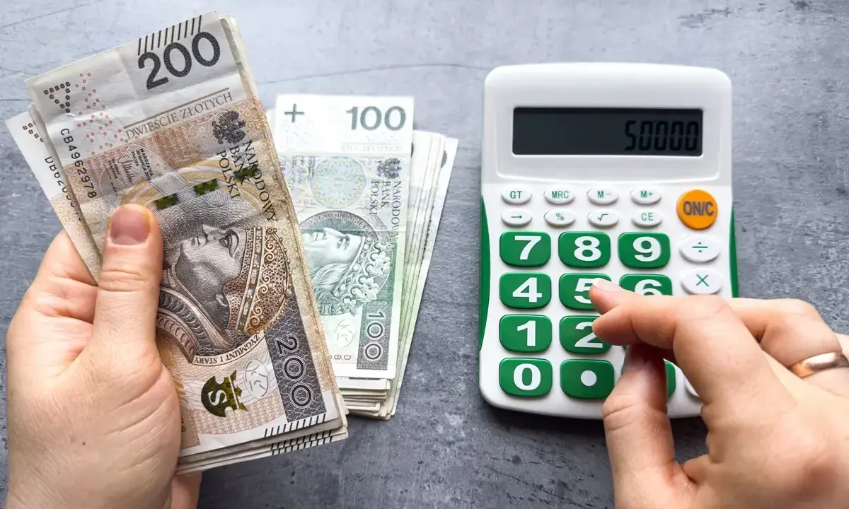 Ręka trzyma banknoty 200 zł i 100 zł, obok kalkulator z wyświetloną kwotą 50000. Czy to już więcej niż minimalna krajowa?
