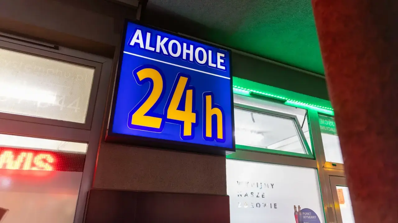Niebieska tablica z napisem "ALKOHOLE 24h" świeci jasno, oferując alkohol mimo potencjalnej prohibicji.
