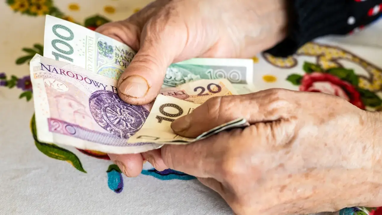 Dłonie starszej osoby liczą pieniądze: 100, 20 i 10 zł. Może to być dodatek opiekuńczy po 80 roku życia.