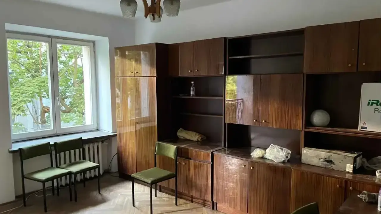 Pokój z meblościanką, oknem i krzesłami. Idealne miejsce na flipowanie mieszkania, by nadać mu nowy blask.
