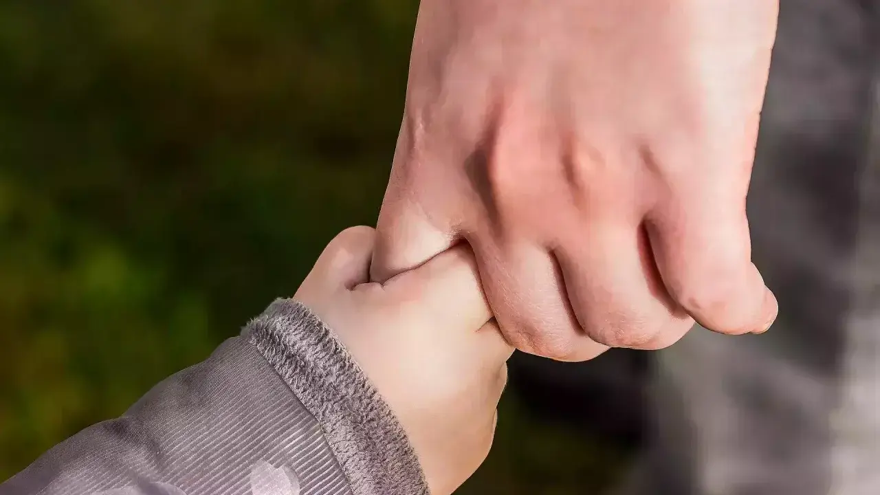 Dłoń dorosłego, opiekuna prawnego, mocno trzyma dłoń dziecka.