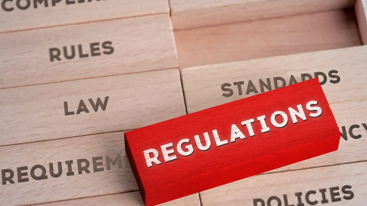 Drewniane klocki z napisami: "Compliance", "Rules", "Law", "Requirements", "Standards", "Policies". Czerwony klocek z napisem "REGULATIONS" wyróżnia się na tle pozostałych, symbolizując kluczowe środki trwałe w biznesie.