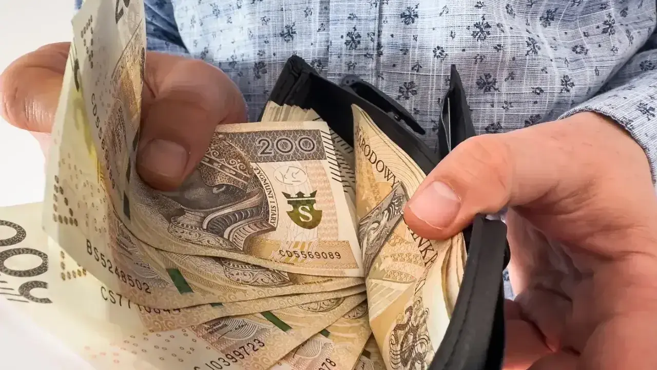 Dłoń pokazuje plik banknotów 200 zł w portfelu. To symbol nagrody jubileuszowej za 40 lat pracy w budżetówce.