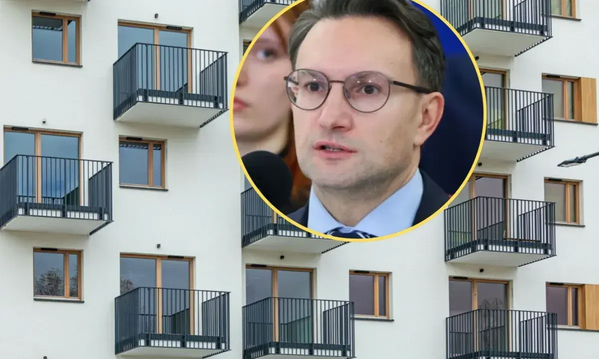 Mężczyzna w okularach przemawia na tle nowoczesnego bloku z balkonami, dyskutując o problemach najmu krótkoterminowego.