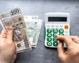 Ręka trzyma banknoty 200 zł i 100 zł, obok kalkulator z wyświetloną kwotą 50000. Czy to już więcej niż minimalna krajowa?