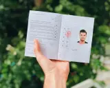 Osoba trzyma dokument z pieczątkami i zdjęciem, wyglądający jak międzynarodowe prawo jazdy.