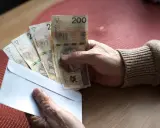 Dłoń trzyma kopertę z banknotami 200 zł. Czy to pieniądze na 800 plus do jakiegoś wieku?