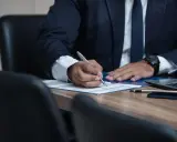 Mężczyzna w garniturze podpisuje dokumenty. Czy to syndyk? Kto to jest?