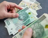 Ręce liczą polskie banknoty 100 zł i 200 zł. Zastanawiasz się, ile wynosi renta rodzinna?