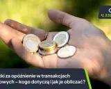Dłoń trzyma monety euro. Tekst informuje o odsetkach za opóźnienie w transakcjach handlowych.