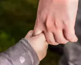 Dłoń dorosłego, opiekuna prawnego, mocno trzyma dłoń dziecka.