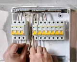 Ręce elektryka podłączają przewody do skrzynki z bezpiecznikami. To właśnie wlz co to za instalacja?