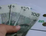 Trzy stuzłotowe banknoty w dłoni, obok dokument ZUS i monety. Czy to 30 krotność zus 2025?