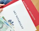Ręka trzyma dokument "Akt notarialny" z banknotami. Kancelaria notarialna przygotowuje ważne dokumenty.