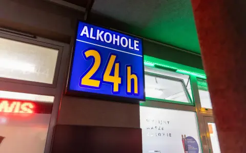 Niebieska tablica z napisem "ALKOHOLE 24h" świeci jasno, oferując alkohol mimo potencjalnej prohibicji.