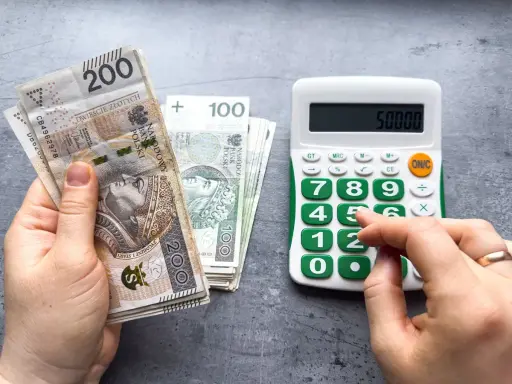 Ręka trzyma banknoty 200 zł i 100 zł, obok kalkulator z wyświetloną kwotą 50000. Czy to już więcej niż minimalna krajowa?