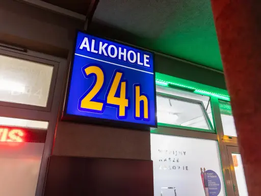 Niebieska tablica z napisem "ALKOHOLE 24h" świeci jasno, oferując alkohol mimo potencjalnej prohibicji.