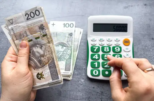 Ręka trzyma banknoty 200 zł i 100 zł, obok kalkulator z wyświetloną kwotą 50000. Czy to już więcej niż minimalna krajowa?