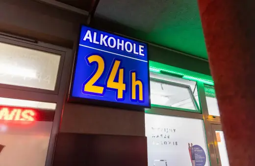 Niebieska tablica z napisem "ALKOHOLE 24h" świeci jasno, oferując alkohol mimo potencjalnej prohibicji.