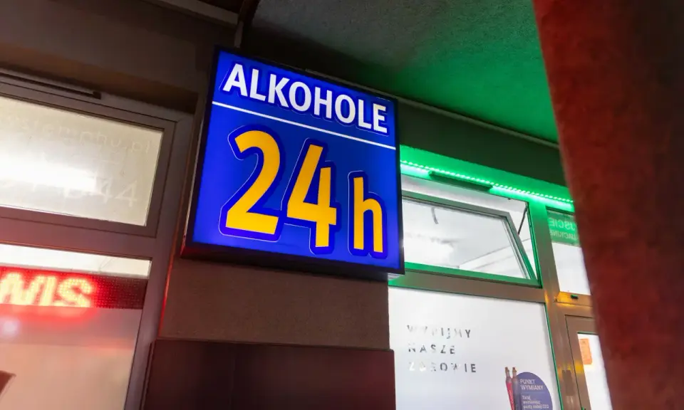 Niebieska tablica z napisem "ALKOHOLE 24h" świeci jasno, oferując alkohol mimo potencjalnej prohibicji.