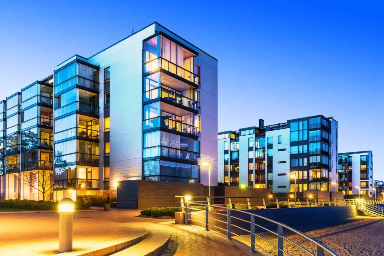 Nowoczesne apartamenty z przeszklonymi balkonami, idealne na najem krótkoterminowy, oświetlone wieczornym blaskiem.