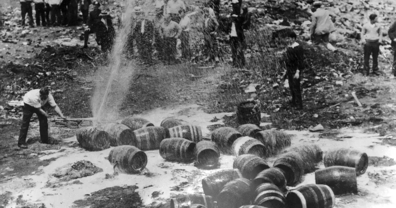 Mężczyzna rozbija beczki z alkoholem, symbolizując koniec prohibicji. W tle widać ludzi i strumień wody.