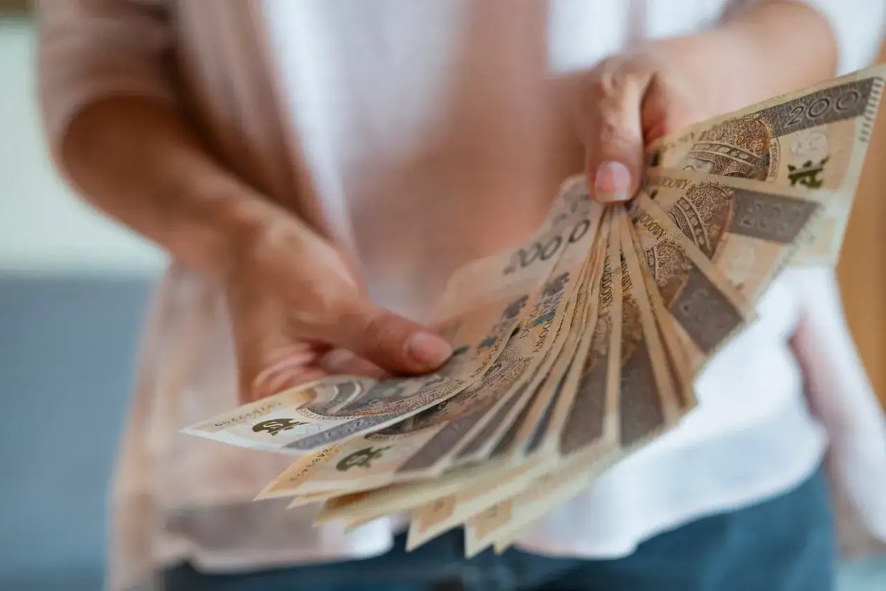 Dłonie trzymają wachlarz banknotów 200 zł. To symbol nagrody jubileuszowej za 40 lat pracy w budżetówce, docenienie wieloletniego stażu.